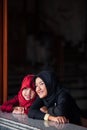 Couple adorable muslim girl in traditional clothing, black and red hijab or niqab and abaya smiling and watching out the window.